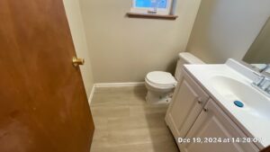 Bathroom Cleaning After - Bio Decon Solutions Small bathroom with a white toilet and white vanity, wood door ajar, and a window above the toilet wall. Date stamp visible in bottom-right corner.