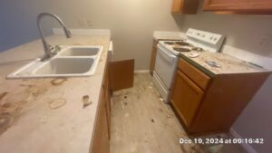 Kitchen Cleaning Before 1 - Bio Decon Solutions Dirty kitchen with stained countertops, double sink, and a worn stove; clutter and debris on the floor and counters, timestamp in bottom corner (Dec 19, 2024 09:16:42).