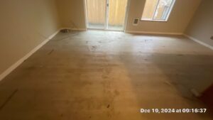 Living Room Cleaning Before - Bio Decon Solutions Small, empty basement room under renovation with bare concrete floor, a sliding glass door to outdoors, a window, and scattered cords and debris on the floor.