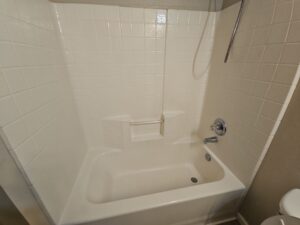 Tub Cleaning After 2 - Bio Decon Solutions White bathtub with tiled surround and built-in corner seat, equipped with a handheld shower head and chrome fixtures.